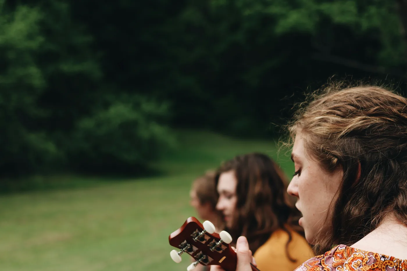 Three young musicians outdoors, singing together while one holds an acoustic guitar