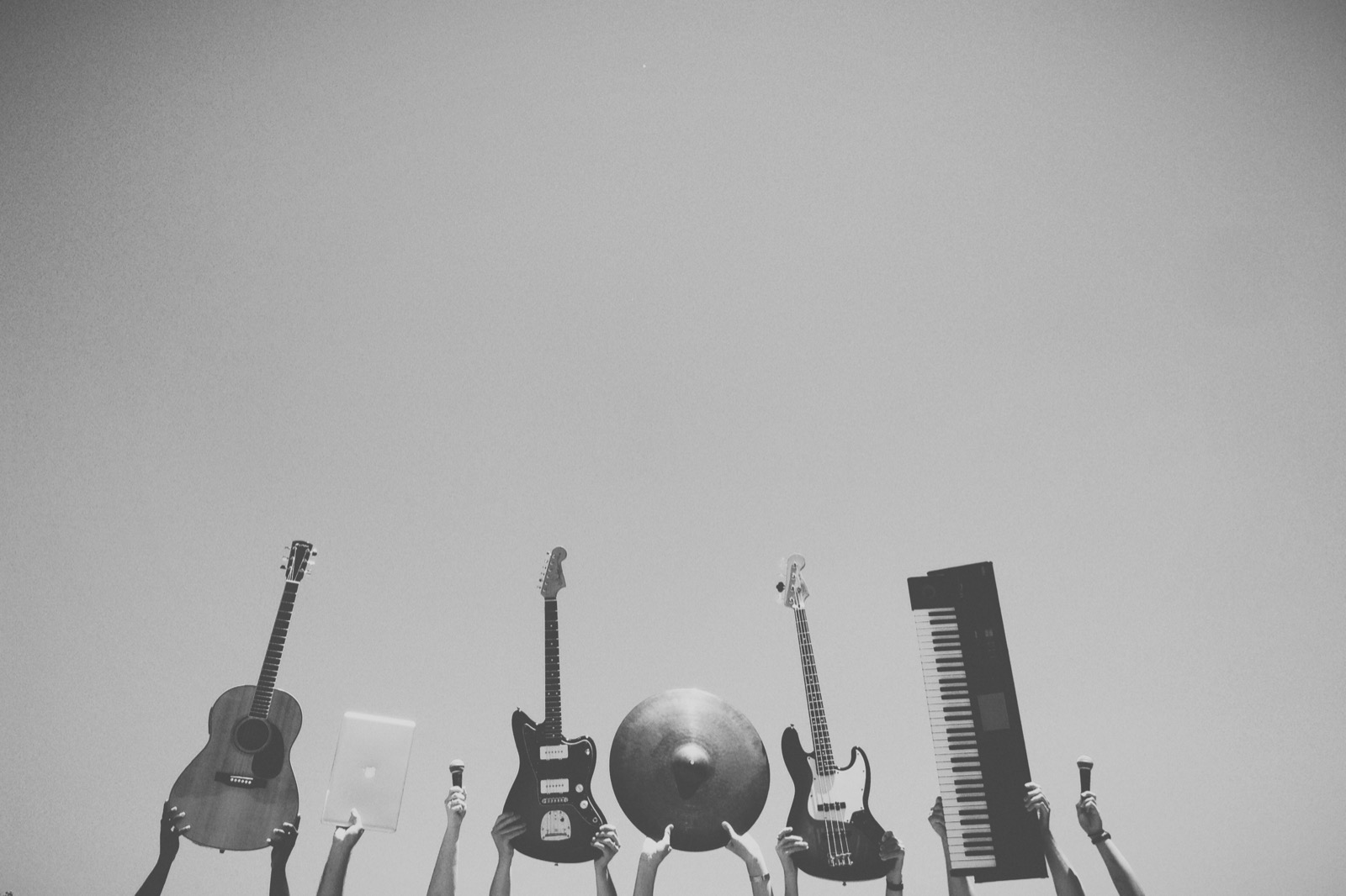 Silhouetted hands holding guitars, a bass, a keyboard, a cymbal and microphones up against the sky